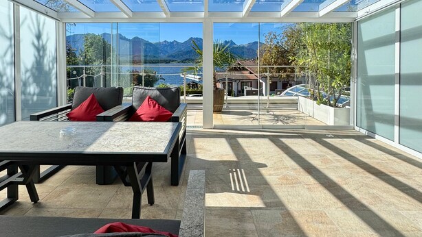 A modern outdoor seating area with a glass ceiling, a table, and a sofa. - Hotel San Marco (Fuessen)