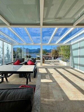 A modern outdoor seating area with a glass ceiling, a table, and a sofa. - Hotel San Marco (Fuessen)