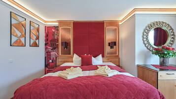 A hotel room with a large bed, red bedding, a wooden headboard, a mirror, and artwork on the walls.