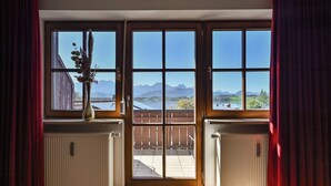 A room with a large window overlooking a deck and mountains. - Hotel San Marco (Fuessen)
