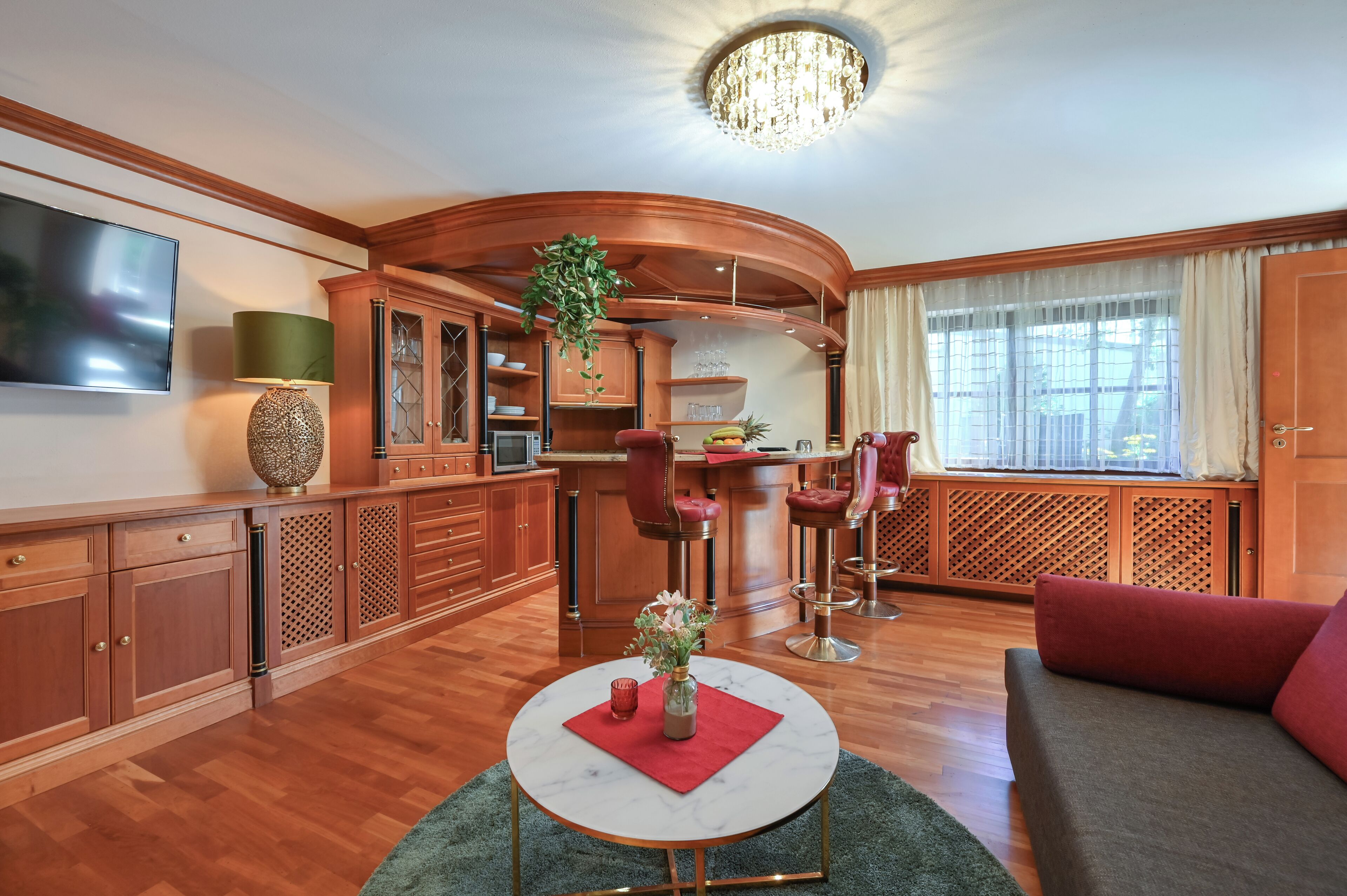 Un salon moderne avec un plancher en bois, une table basse ronde, un canapé, un téléviseur fixé au mur et un coin cuisine avec un bar.