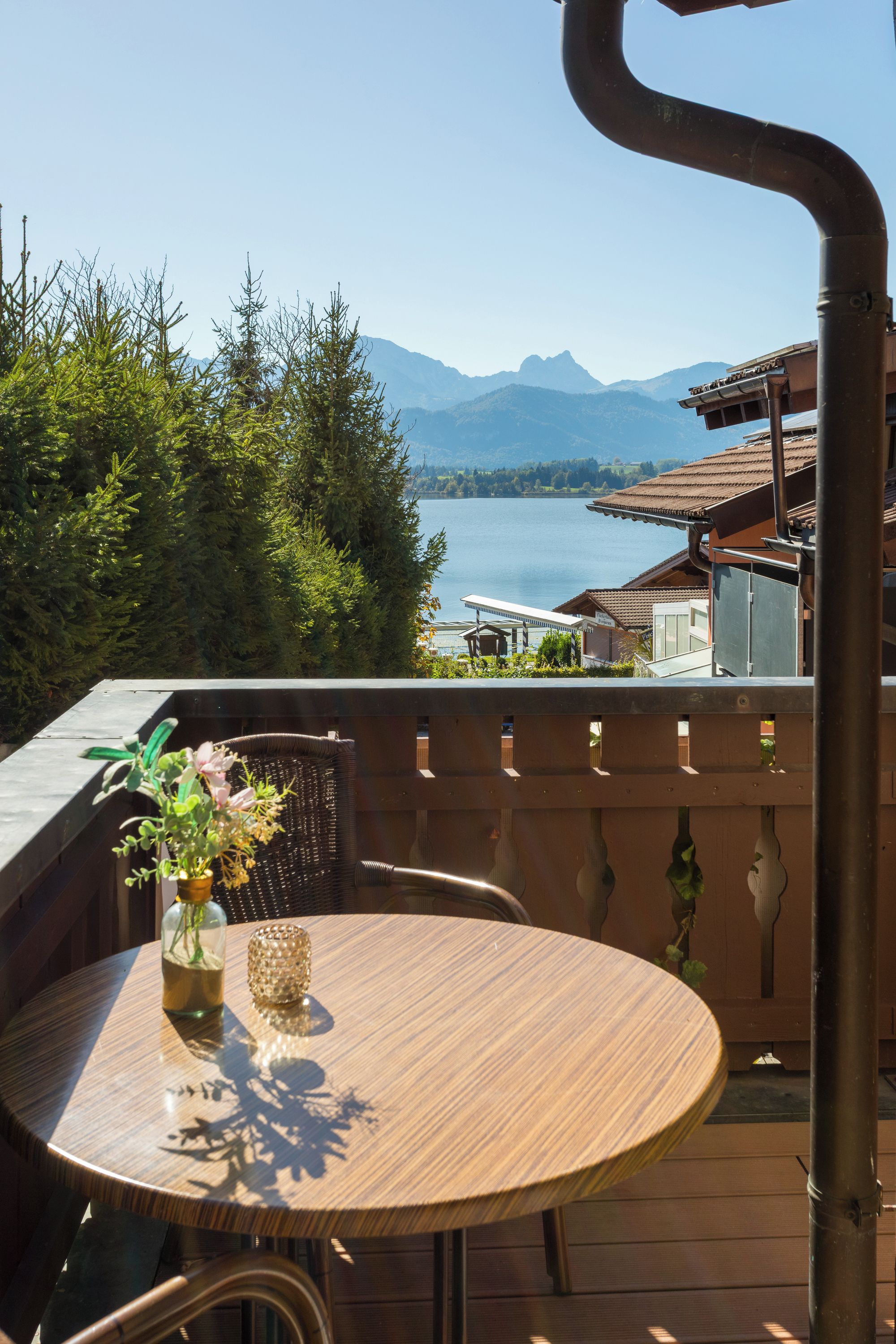 Ein runder Holztisch mit einer Vase und Kerze auf einem Balkon mit Blick auf einen See und Berge.