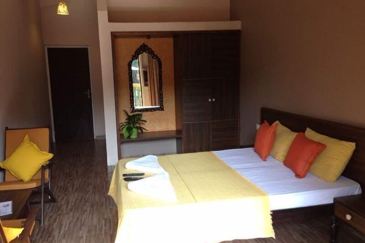 A hotel room with a bed, a desk, a chair, a mirror, and a potted plant.