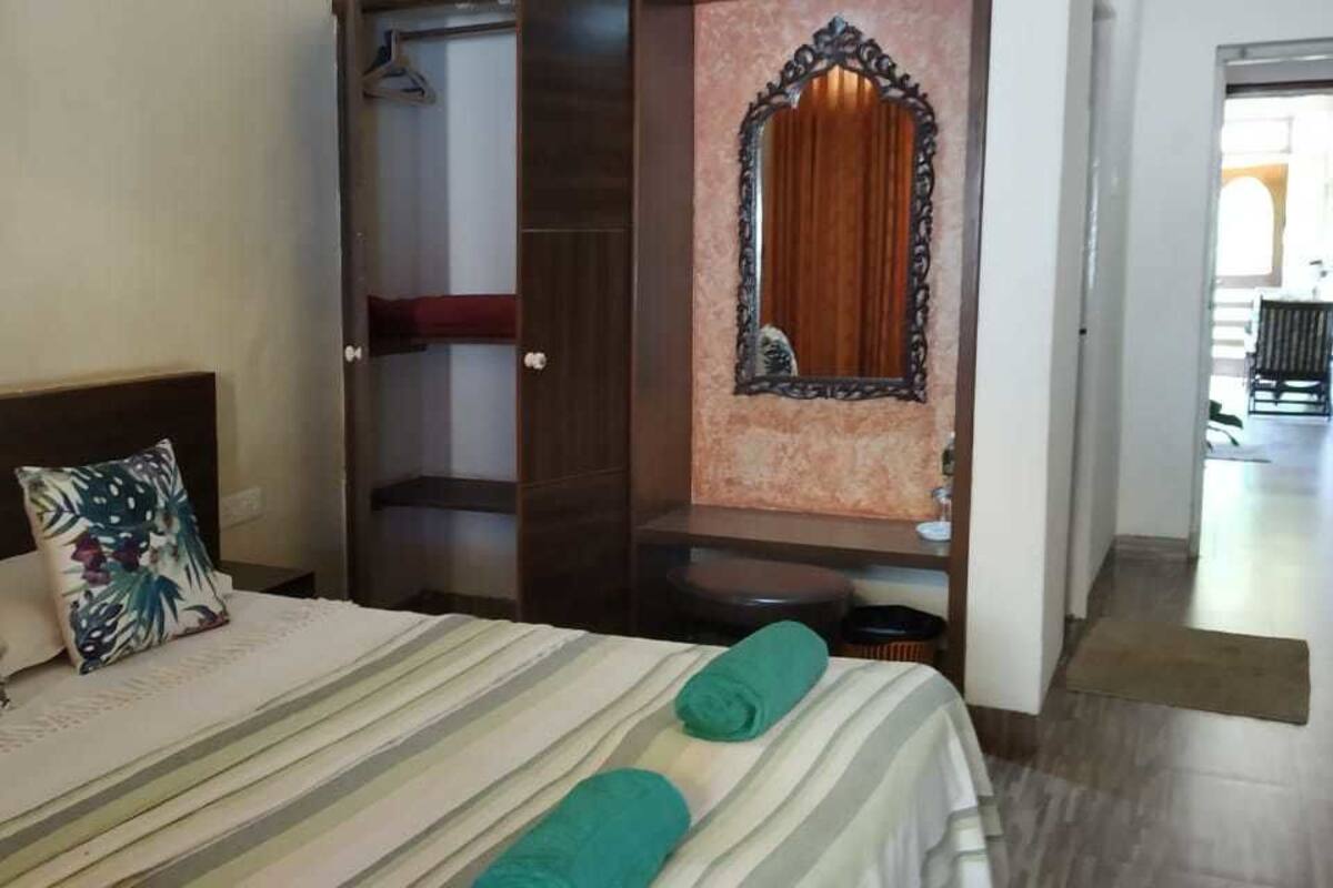 A hotel room with a bed, a wardrobe, a mirror, and a door leading to another room.
