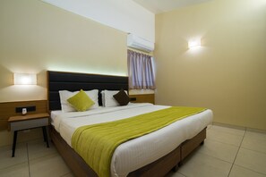 A neatly made bed with a green blanket, a bedside table with a lamp, and a wall-mounted air conditioner. - So My Resort (Calangute)
