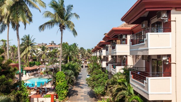A hotel with multiple balconies, a swimming pool, and lush greenery. - So My Resort (Calangute)
