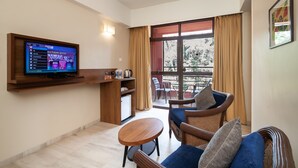 A modern living room with a flat-screen TV, a small kitchenette, a dining area, and a balcony with a view. - So My Resort (Calangute)
