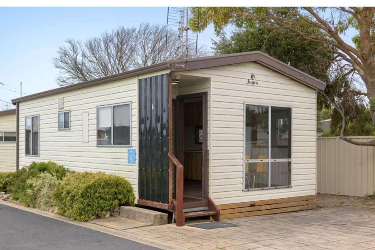 A single-story mobile home with a brown door and windows, a small porch, and a number '5' sign.