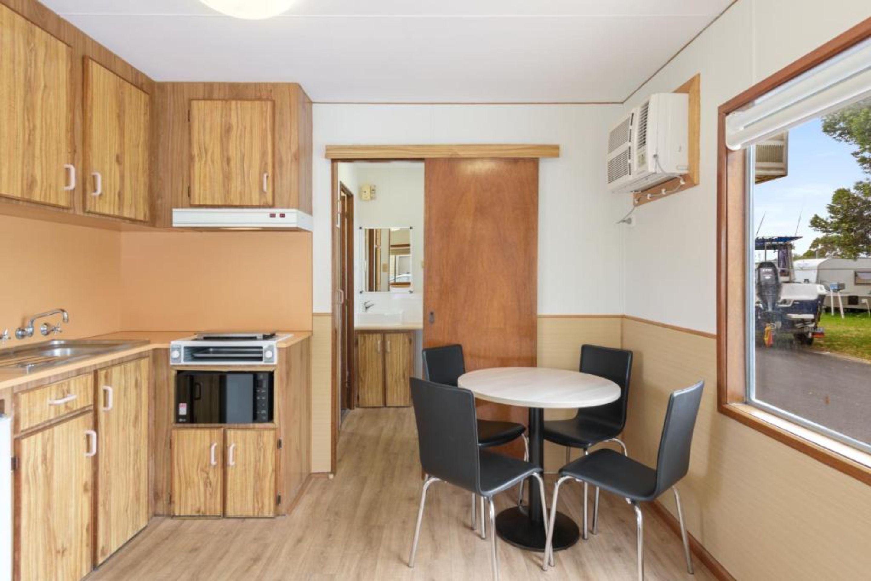 A compact kitchen with wooden cabinets, a microwave, and a small dining area with a round table and four chairs.
