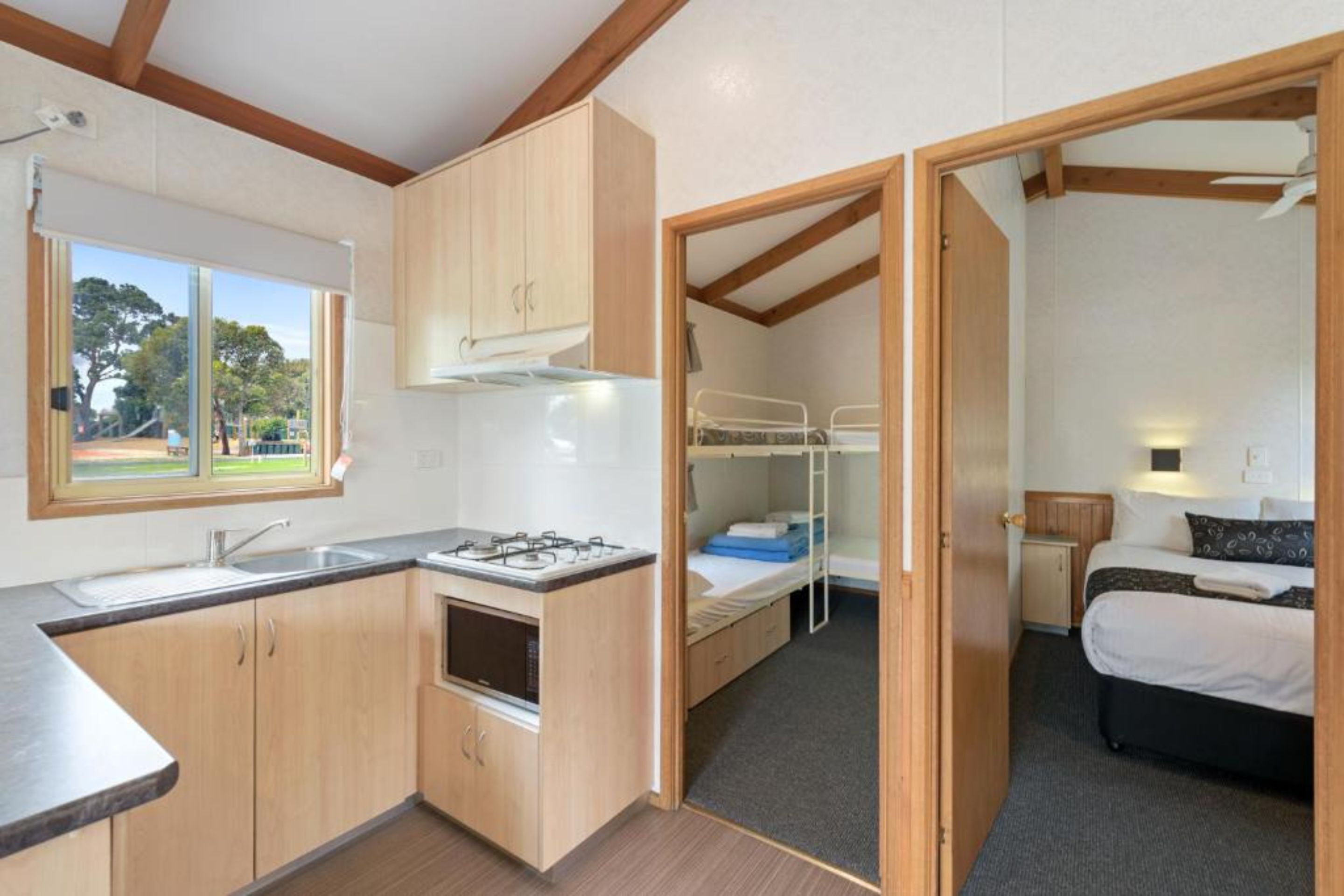 Una habitación compacta con kitchenette, una cama individual superpuesta y ventana con vista a árboles.