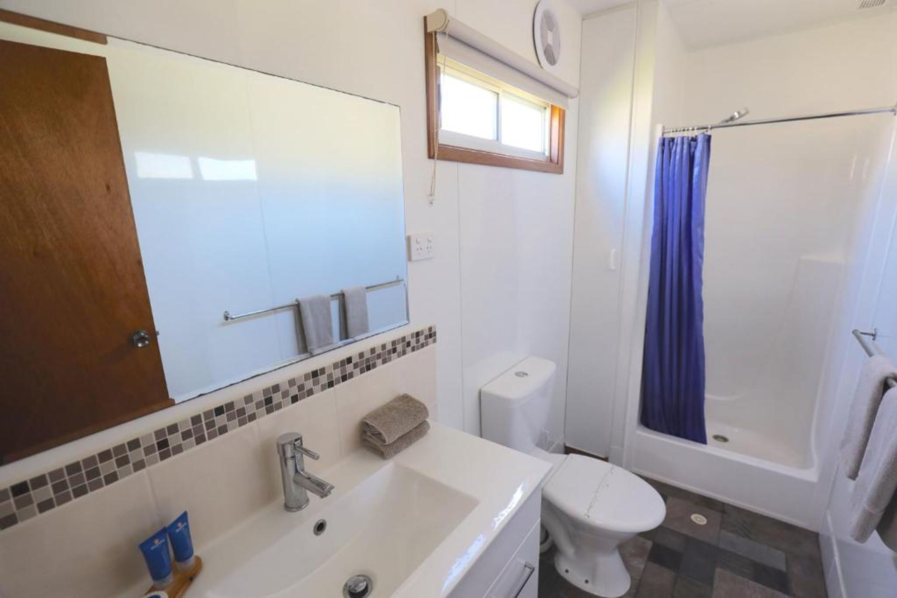 Une salle de bain avec un lavabo, des toilettes et une douche, le tout de couleur blanche.