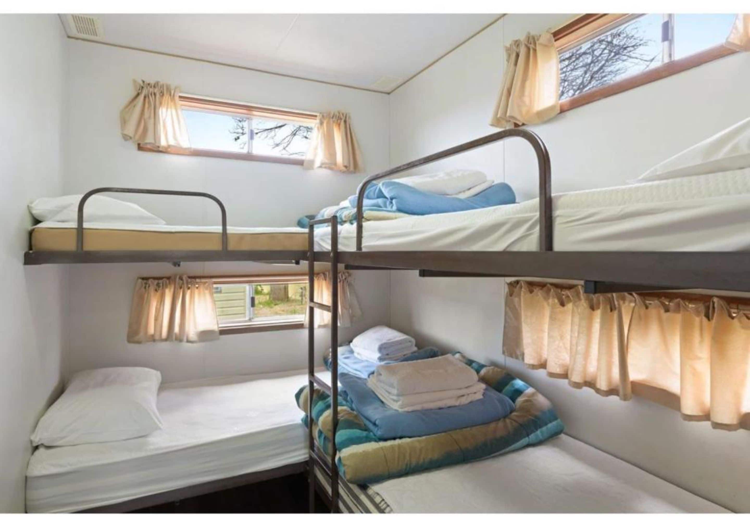 A dormitory room with bunk beds, a window with curtains, and a small table.