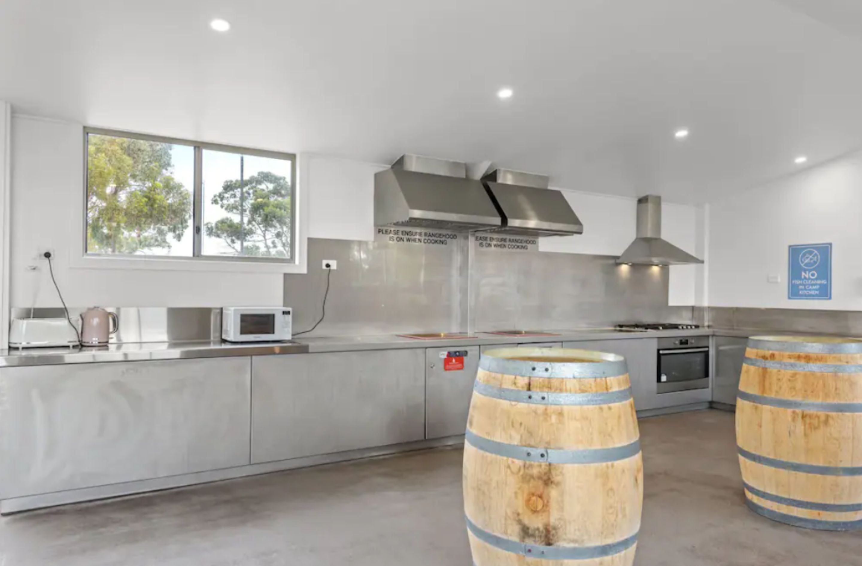 A modern kitchen with stainless steel appliances, a large window, and two wooden barrels.