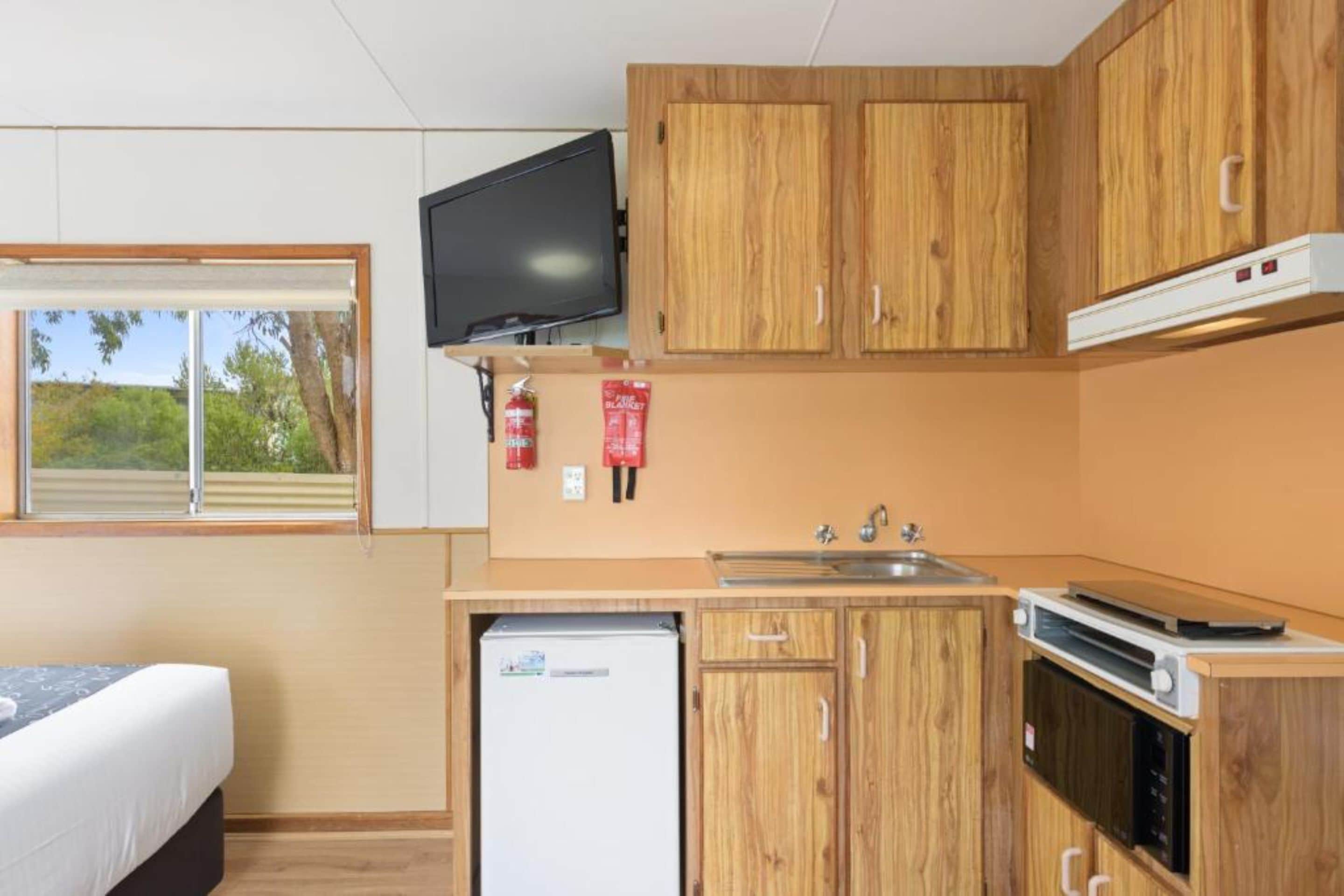Una cocina compacta con armarios de madera, horno integrado, refrigerador y ventana con vistas al verdor.