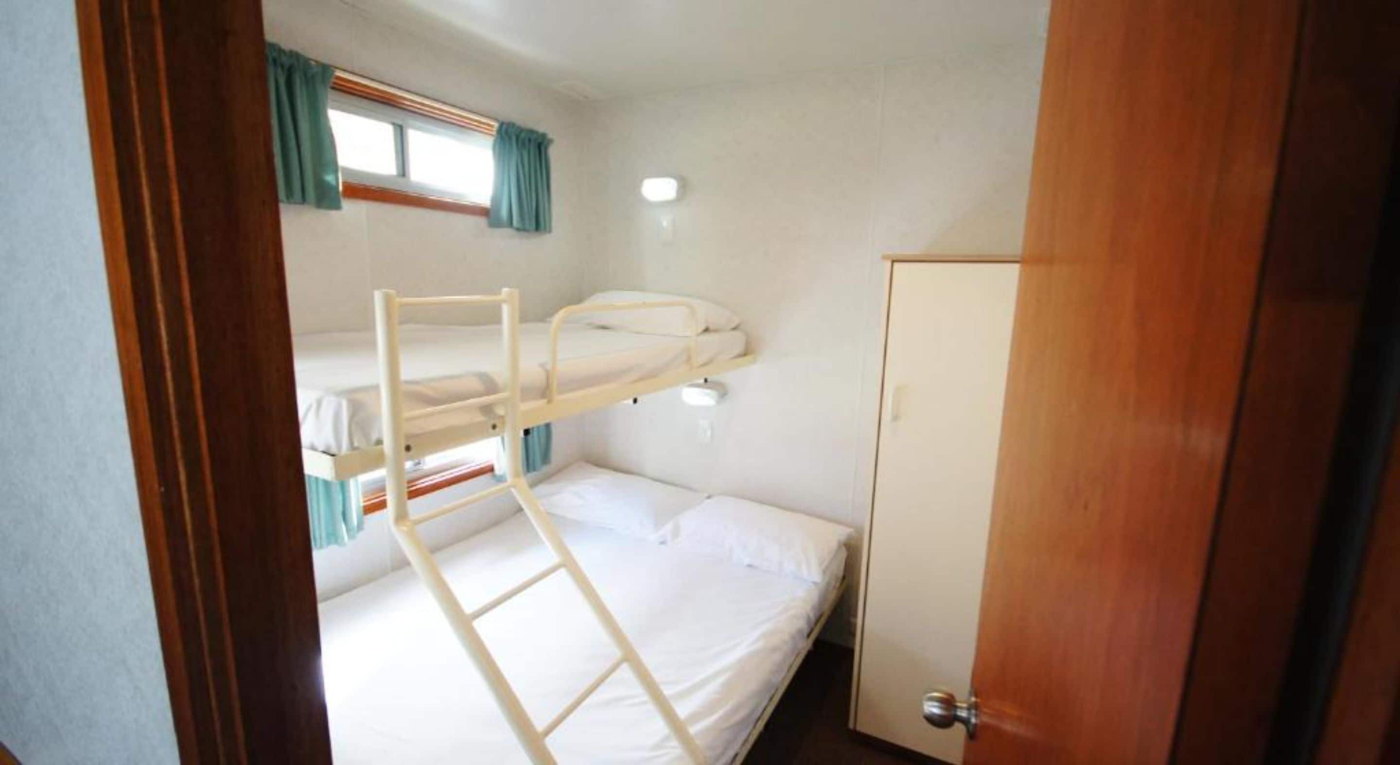 A bunk bed room with a wooden ladder, a single bed, and a door.