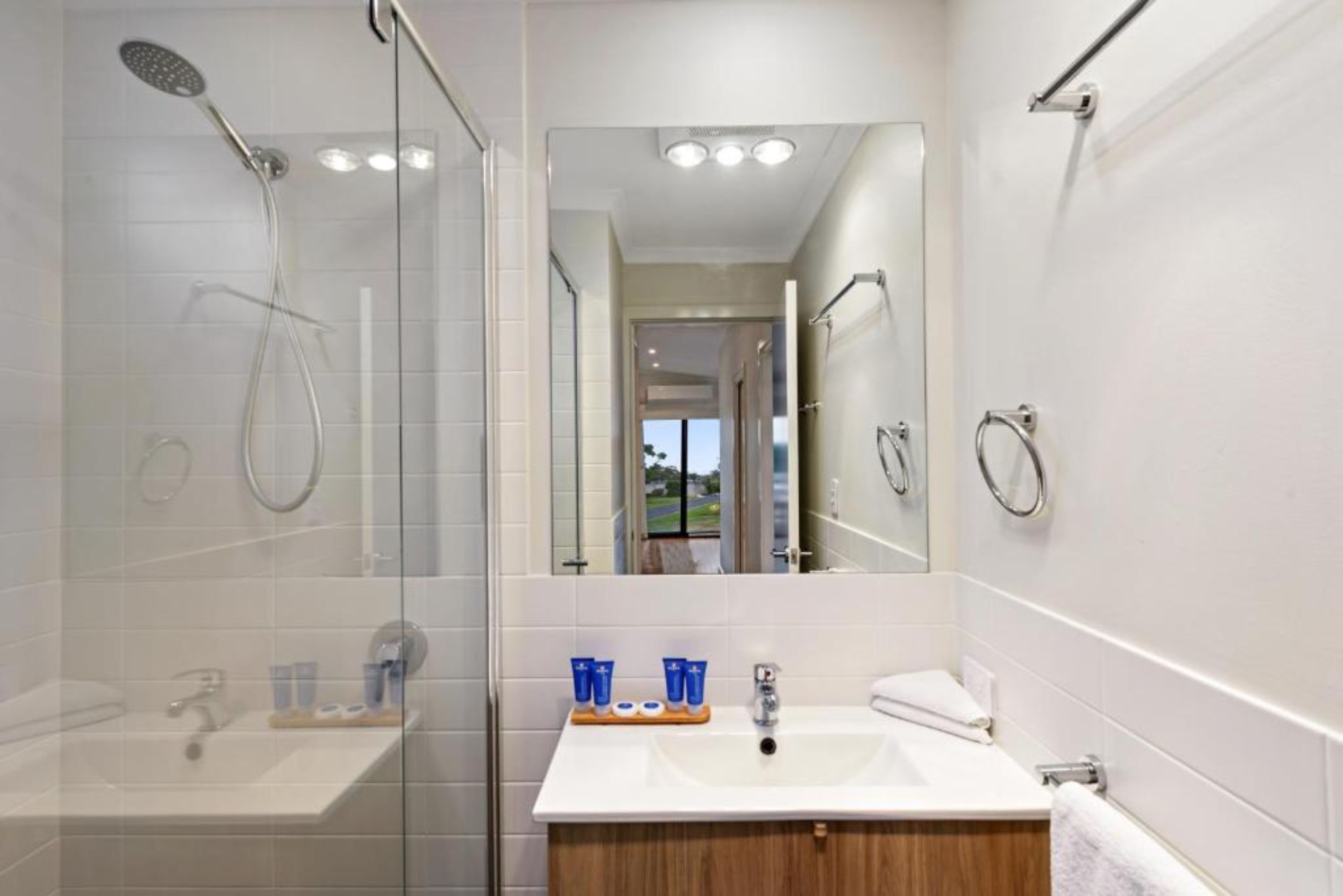 Une salle de bain moderne avec une douche à parois de verre, un lavabo blanc avec un meuble-vasque en bois et un grand miroir.