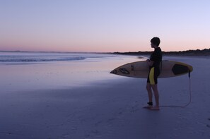A person holding a surfboard on a beach at sunset.