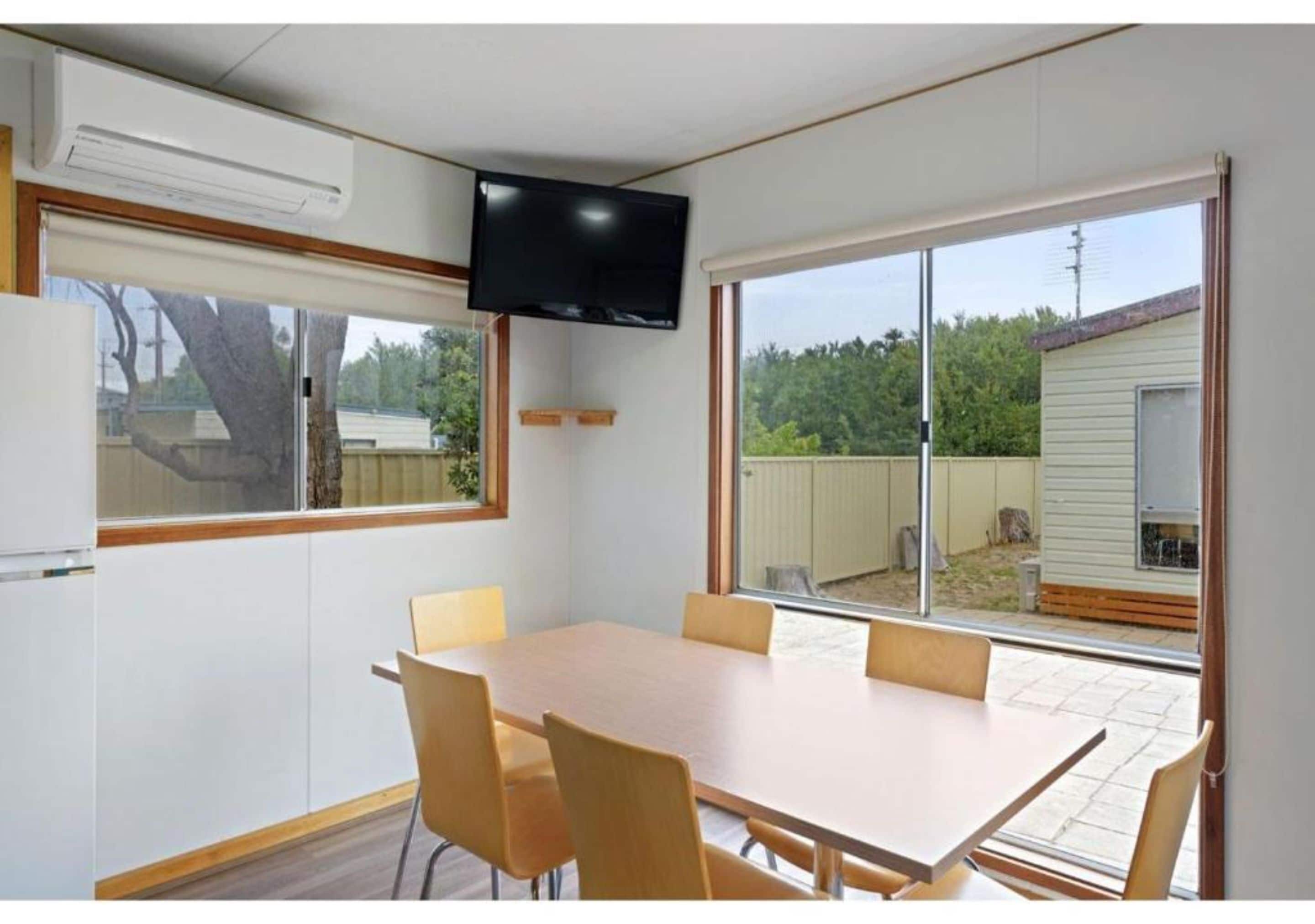 A room with a large table and chairs, a flat-screen TV mounted on the wall, and a sliding glass door leading to an outdoor area.