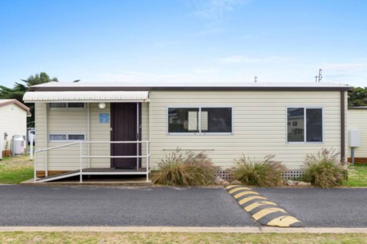 A single-story mobile home with a front porch, a small ramp, and a driveway with a curb.