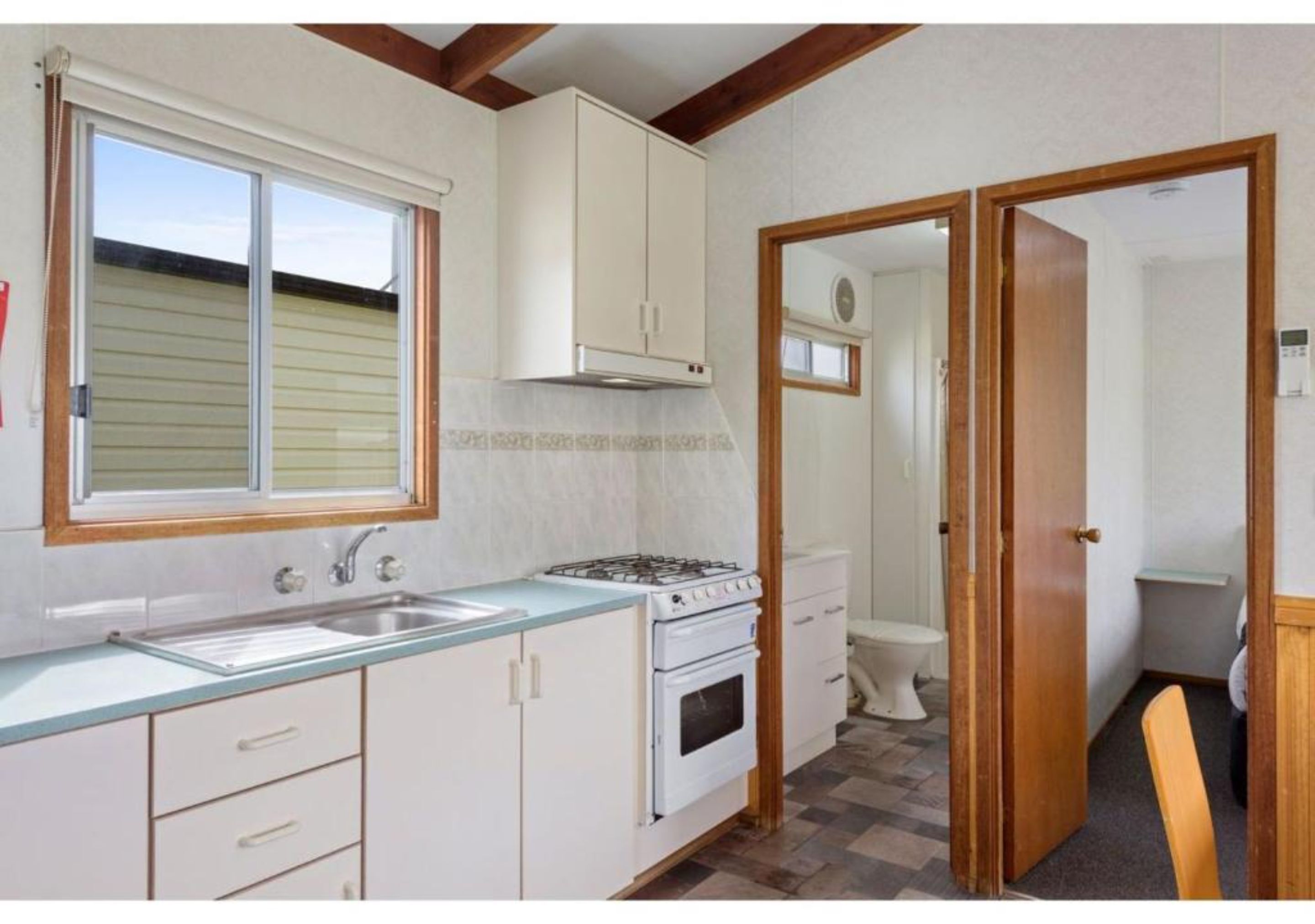 A compact kitchen with a gas stove, oven, and sink, wooden cabinets, and a window.
