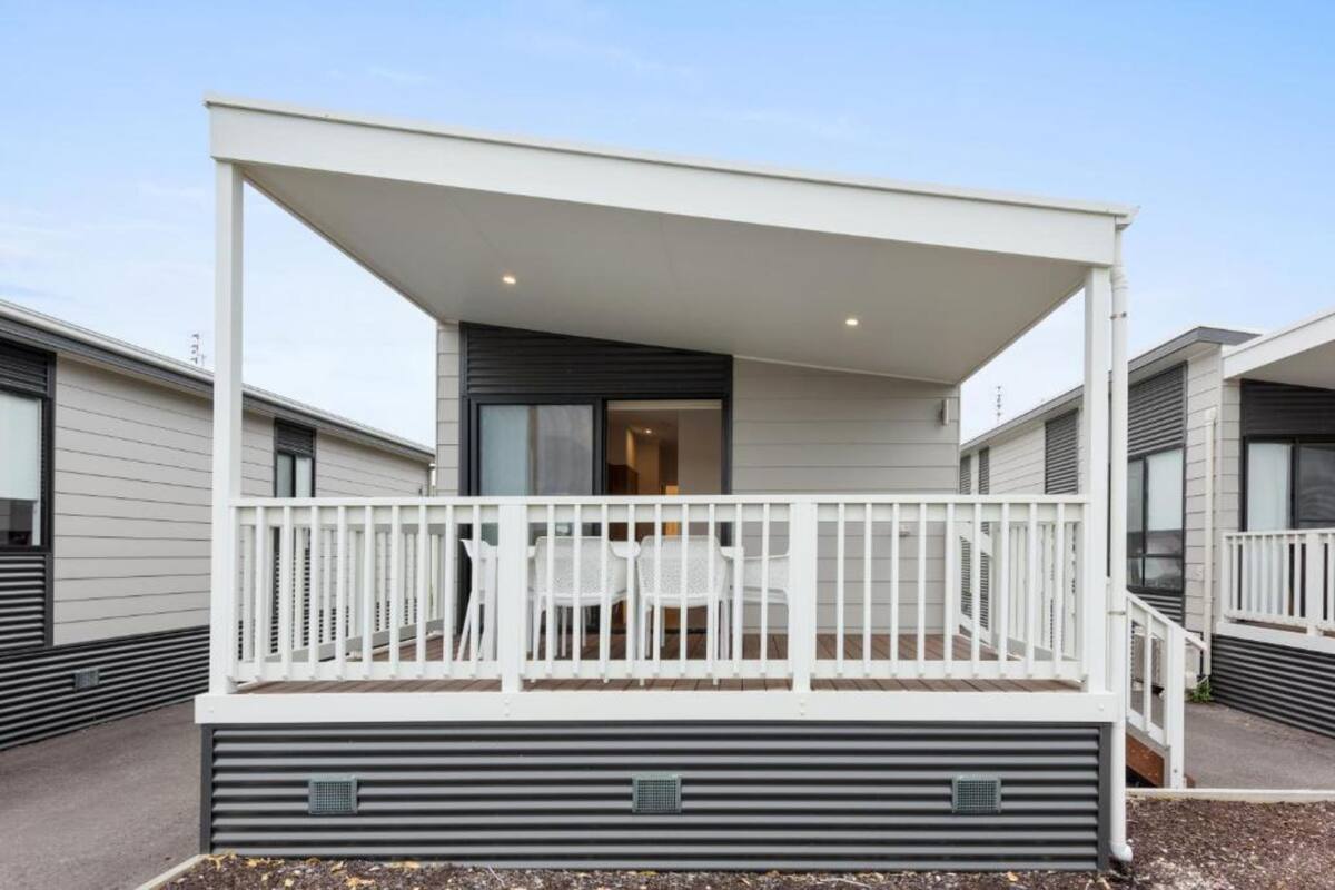 A modern outdoor balcony with a white railing, a table, and chairs.