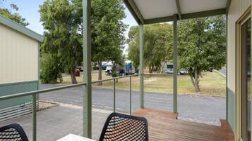 A covered outdoor area with a table and chairs, a view of parked vehicles, and trees in the background.