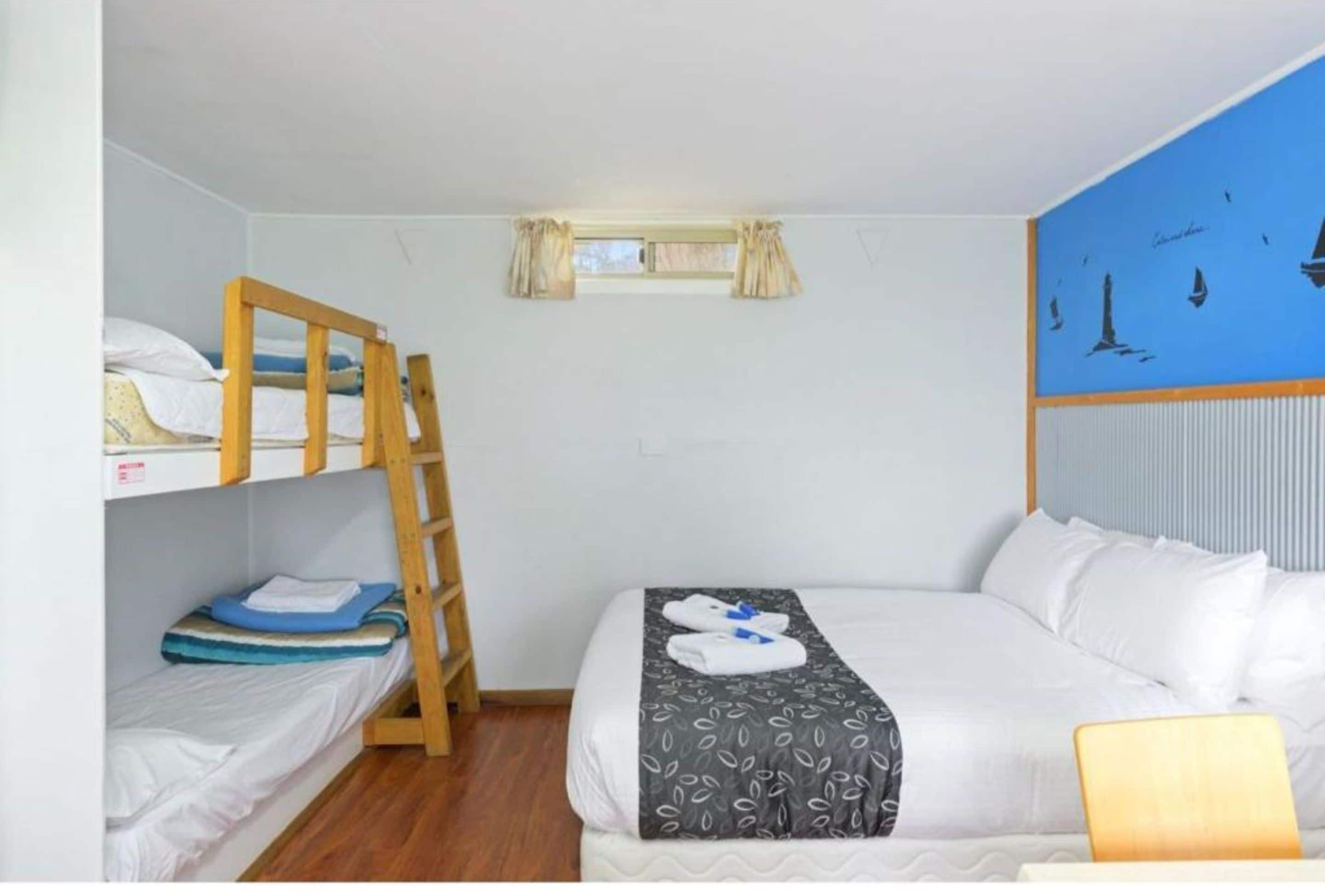 Una habitación con literas, una cama individual, una ventana con cortinas y un mural de un velero en la pared.