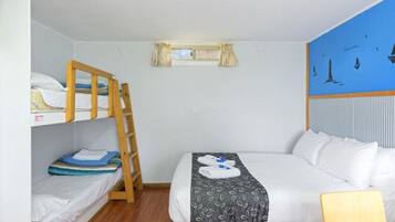 Una habitación con literas, una cama individual, una ventana con cortinas y un mural de un velero en la pared.