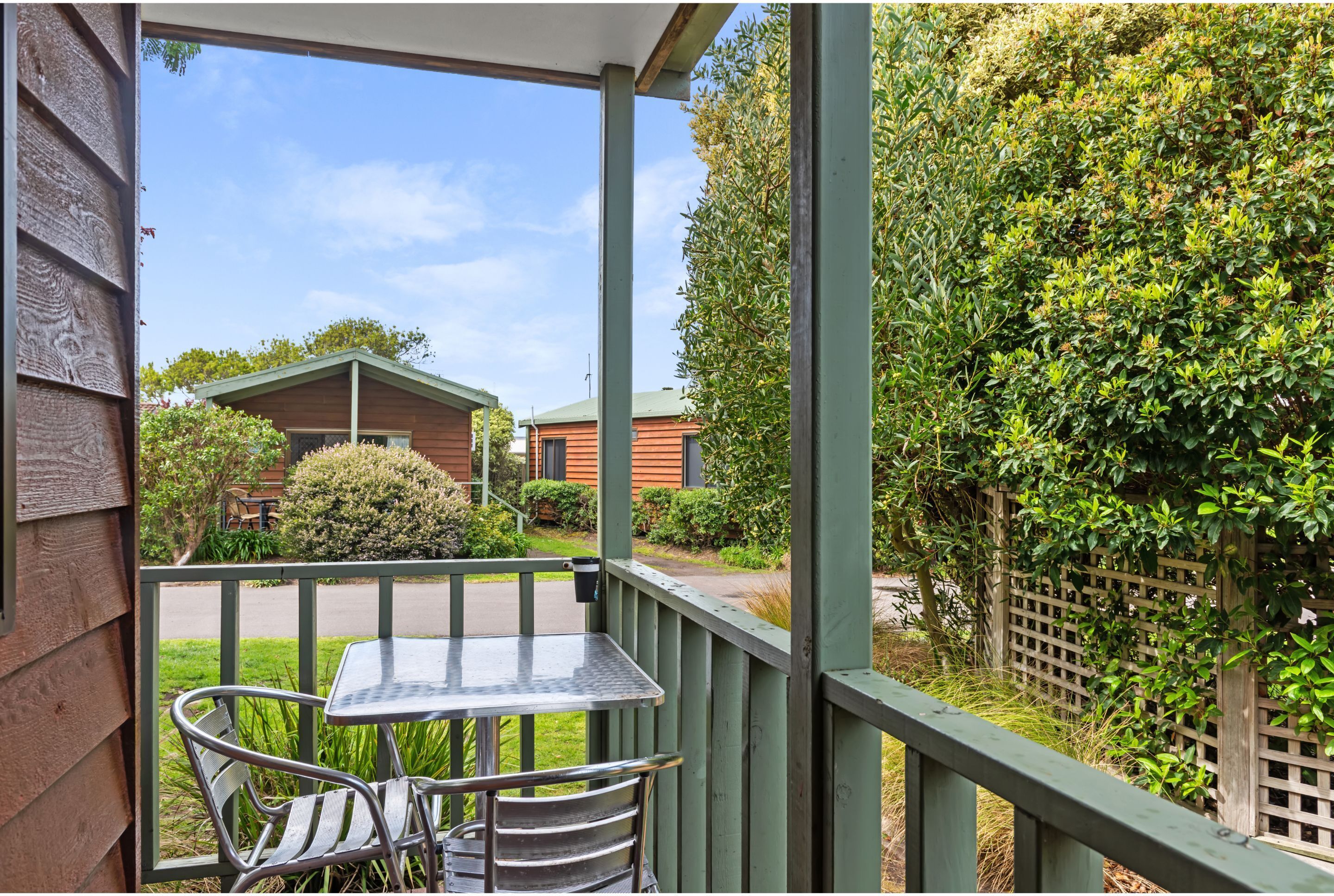 A covered outdoor area with a table and chairs, a wooden fence, and a view of a house and greenery.