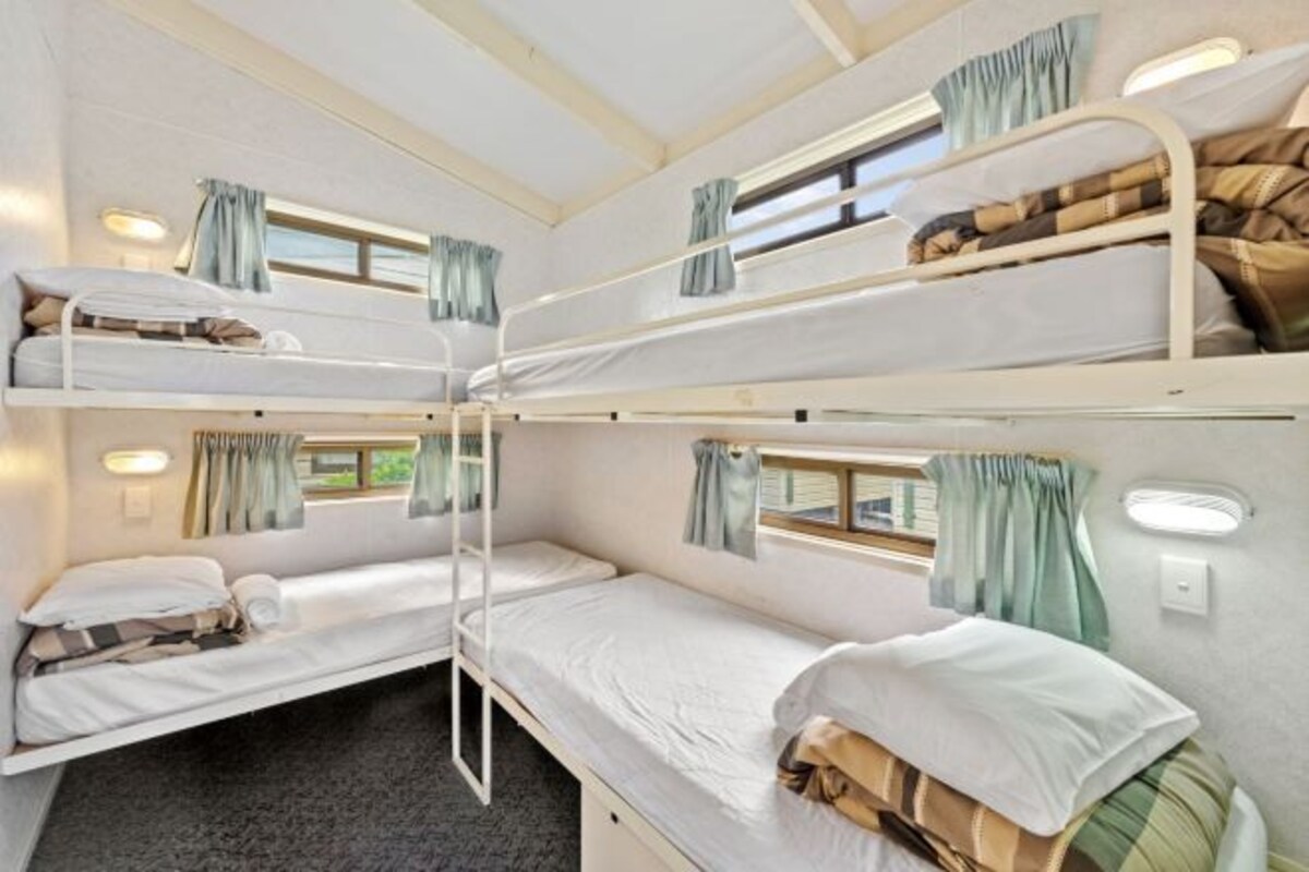 Um dormitório com três andares de camas, cada uma com janela e cortinas.