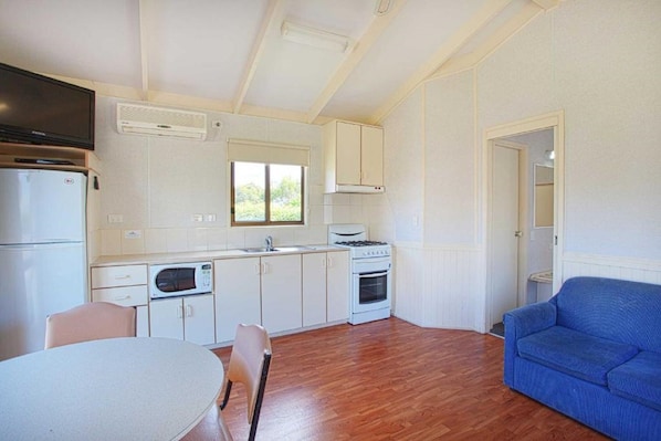A compact kitchen with white cabinets, a microwave, a stove, and a window.