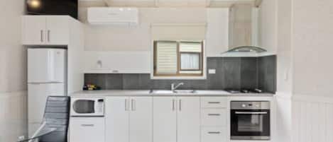 A compact kitchen with white cabinetry, a microwave, a stove, and a sink.