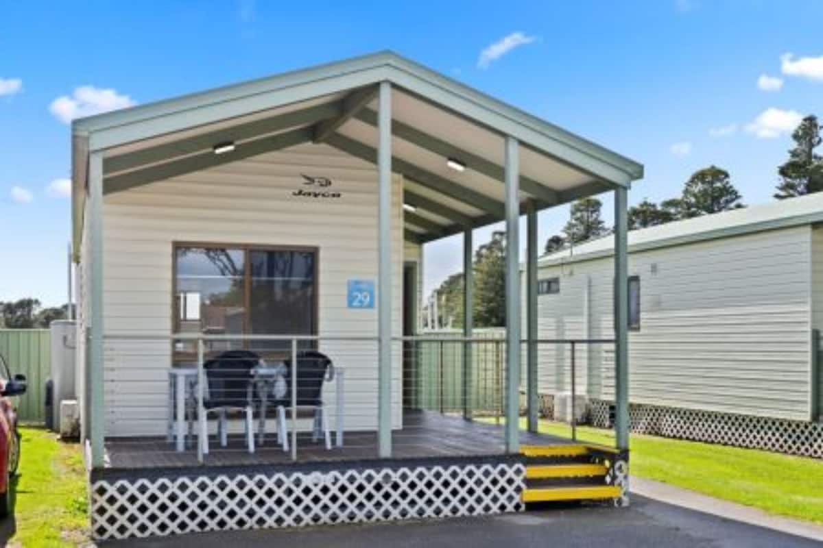 A single-story mobile home with a covered porch, a small table and chairs, and a number '29' sign.
