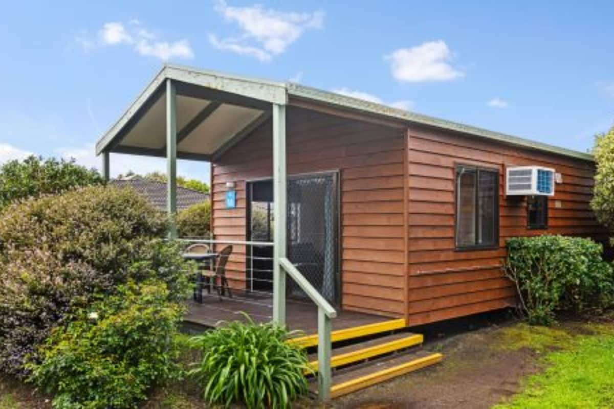 A small wooden cabin with a covered porch, a window, and an air conditioning unit.