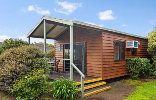 A small wooden cabin with a covered porch, a window, and an air conditioning unit.