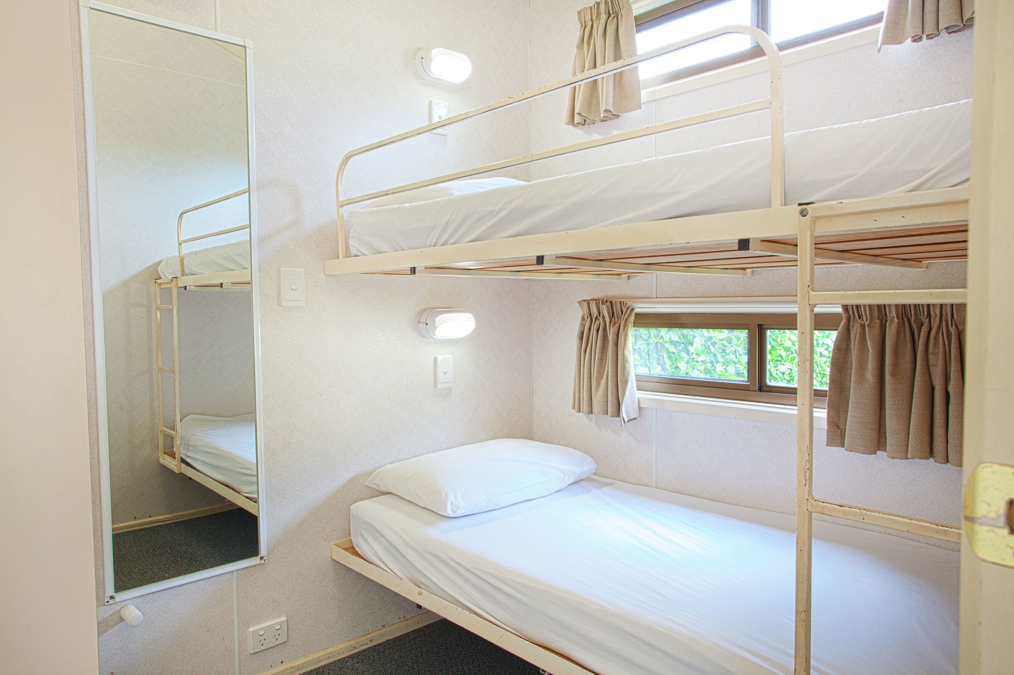 A bunk bed room with a mirror, a window with curtains, and a light switch.