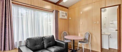 A room with a black leather sofa, a small round table with two chairs, wooden walls, and a door.