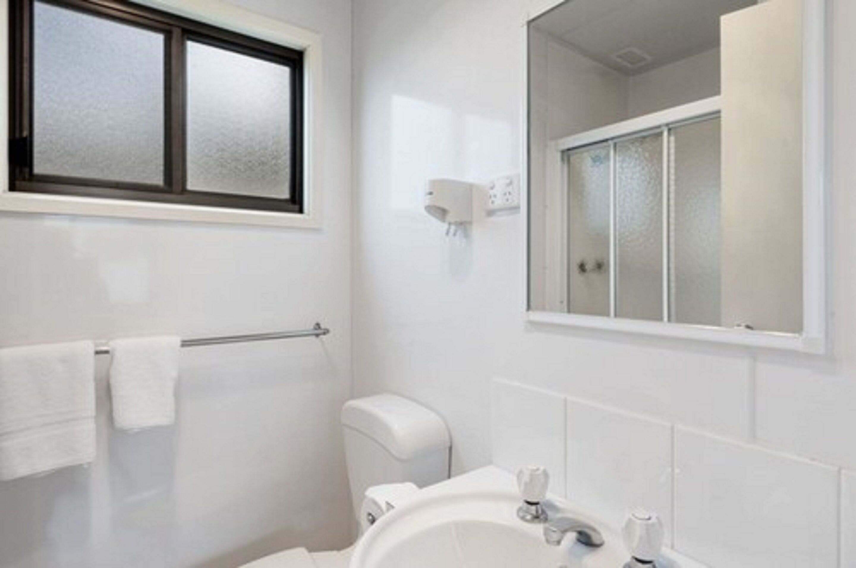 Un bagno con lavandino bianco, un water, portasci e una finestra con vetro satinato.