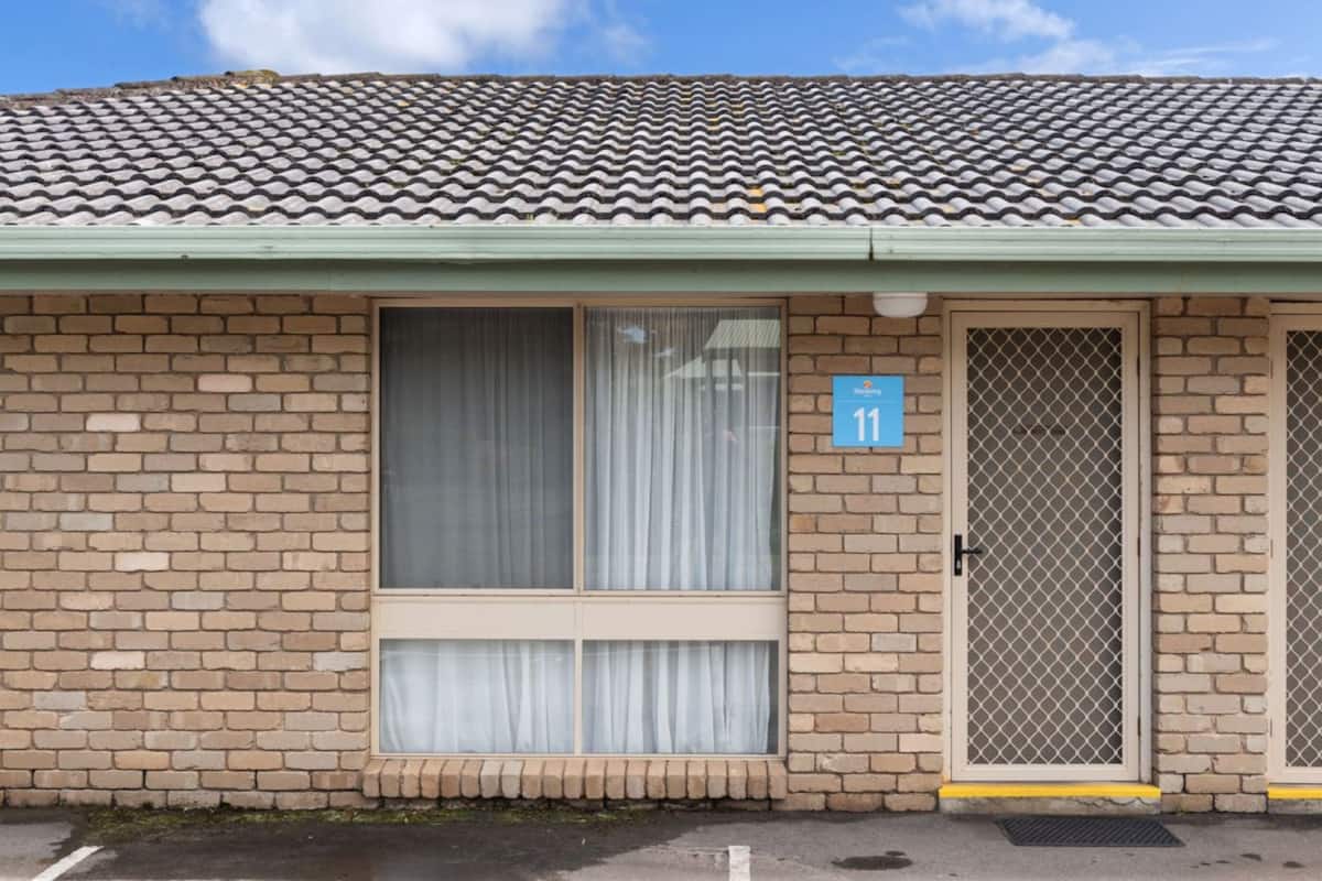 A brick building with a tiled roof, a large window with curtains, a door with a mesh screen, and a blue sign with the number 11.
