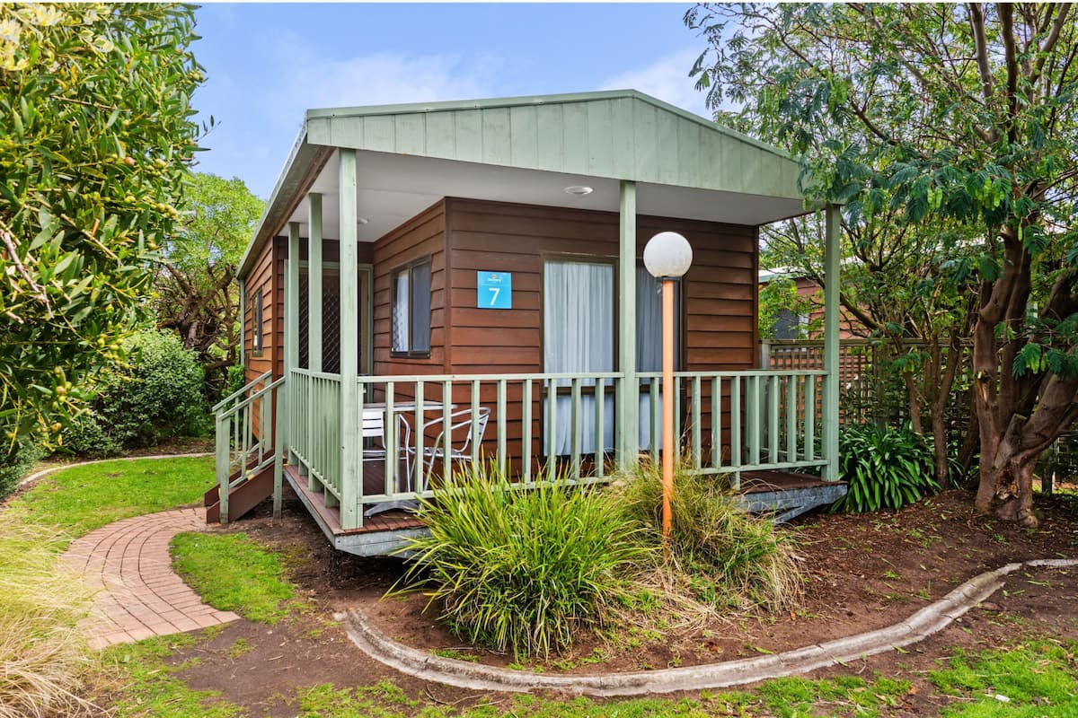 A small, single-story wooden cabin with a porch, number 7, surrounded by lush greenery.
