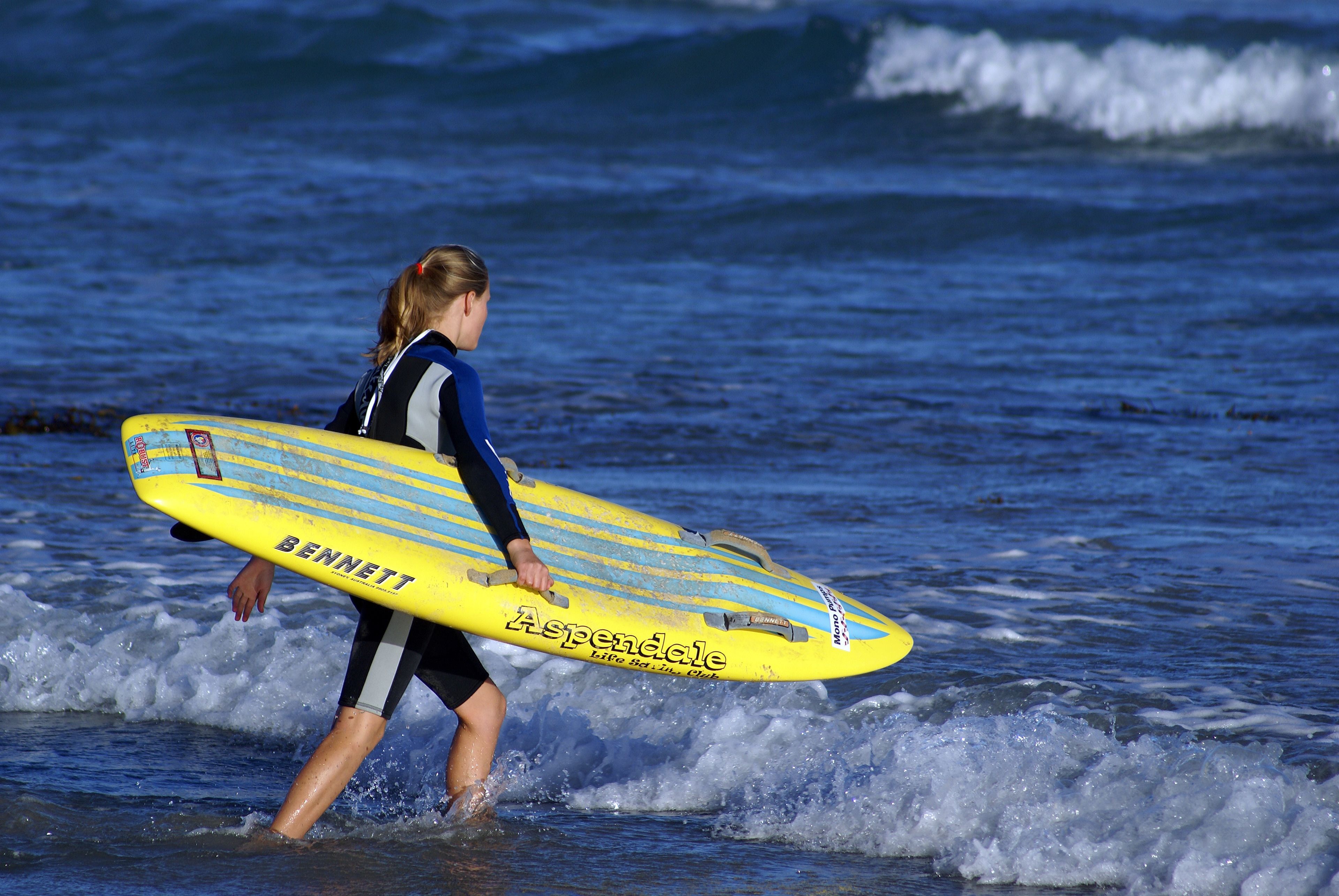 A person carrying a yellow surfboard with text on it.