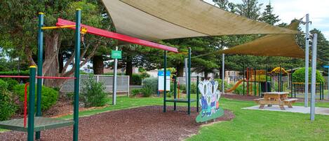 Un parque infantil con tobogán, columpios y una mesa de picnic.