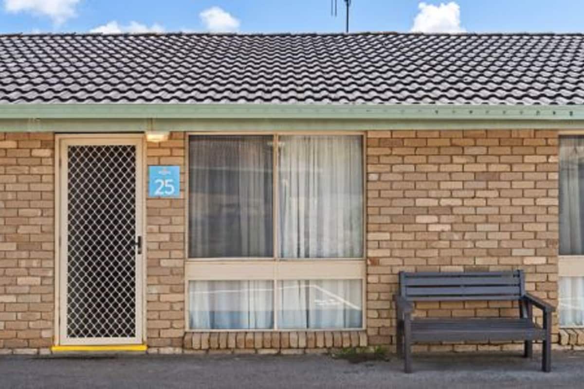 A single-story brick building with a tiled roof, a numbered door, and a bench outside.