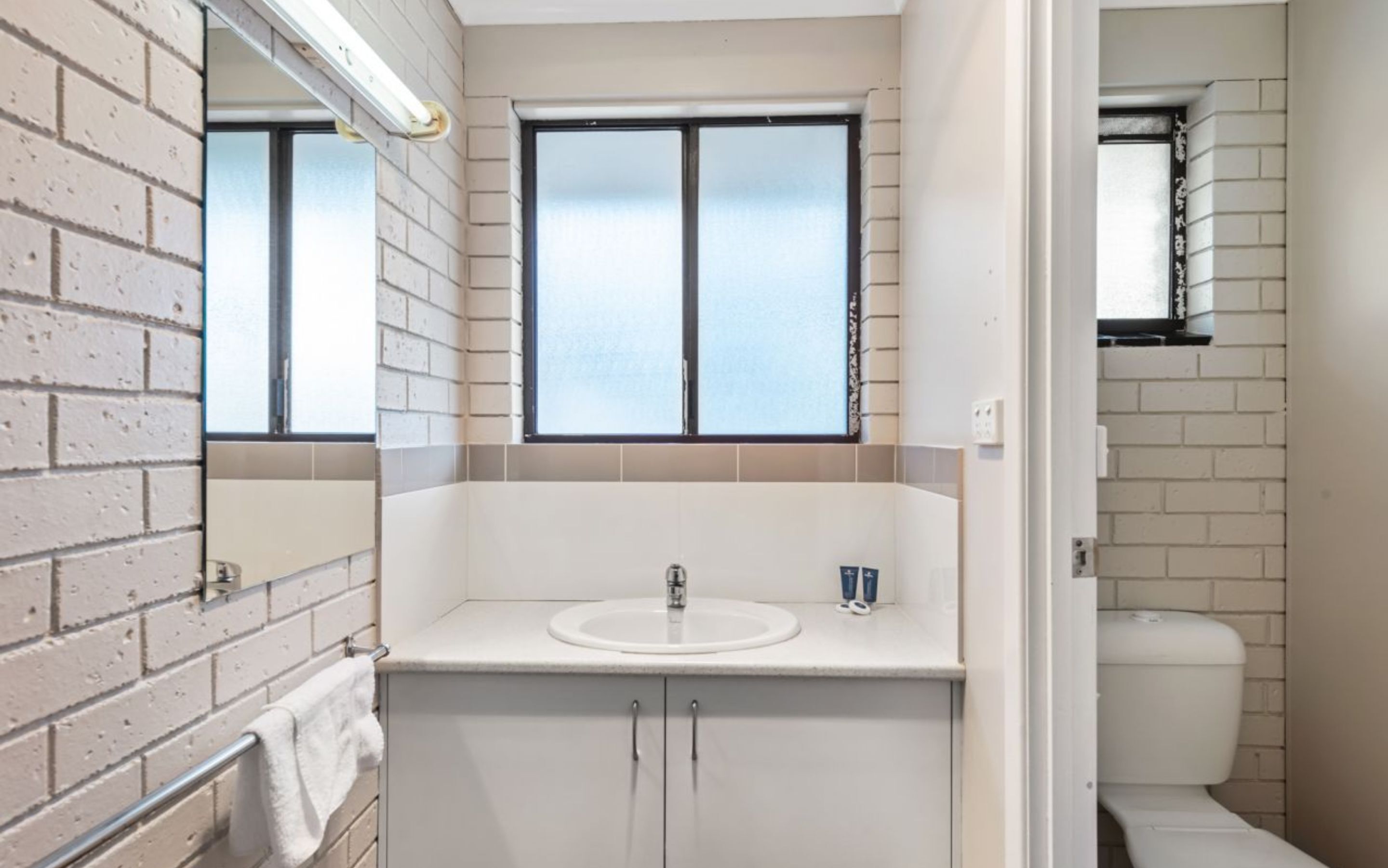 Een badkamer met een wit wastafel, een spiegel en een raam.