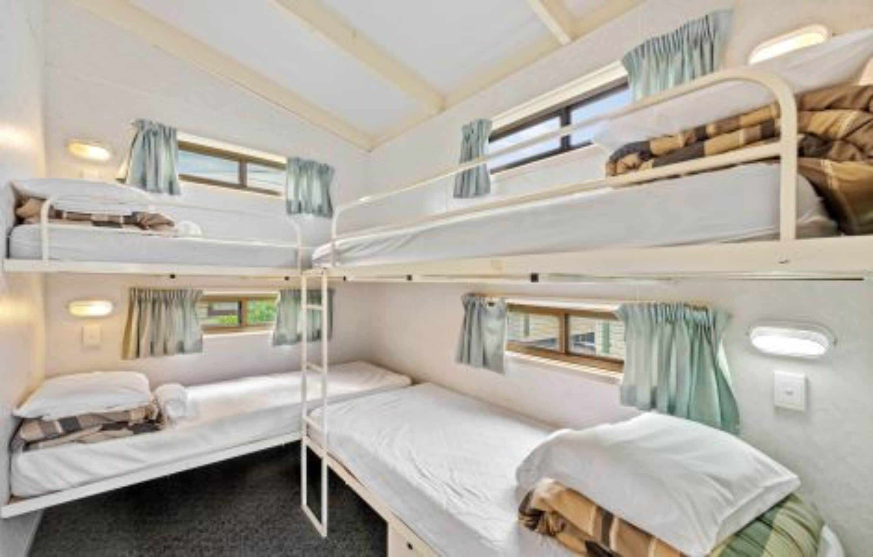 A bunk bed room with two beds, each with a window and curtains.