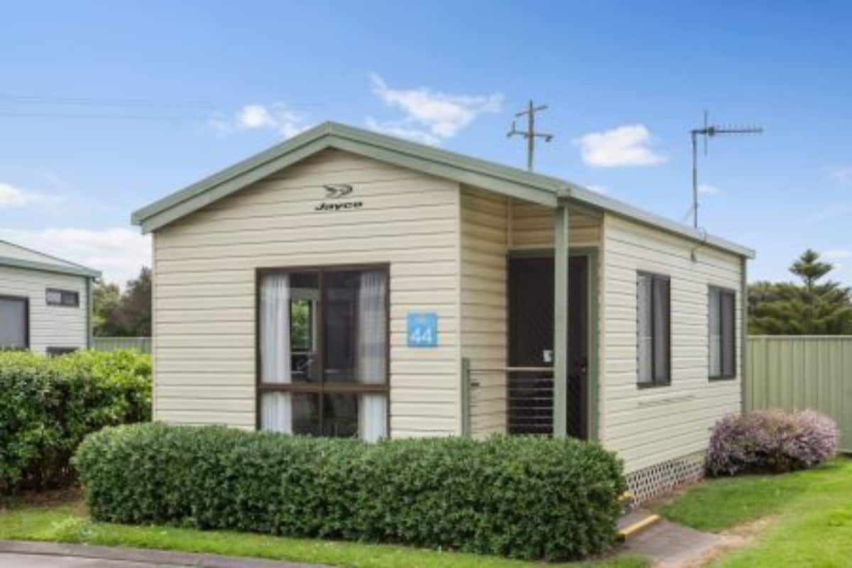 A single-story mobile home with a pitched roof, a small porch, and a number '44' sign.