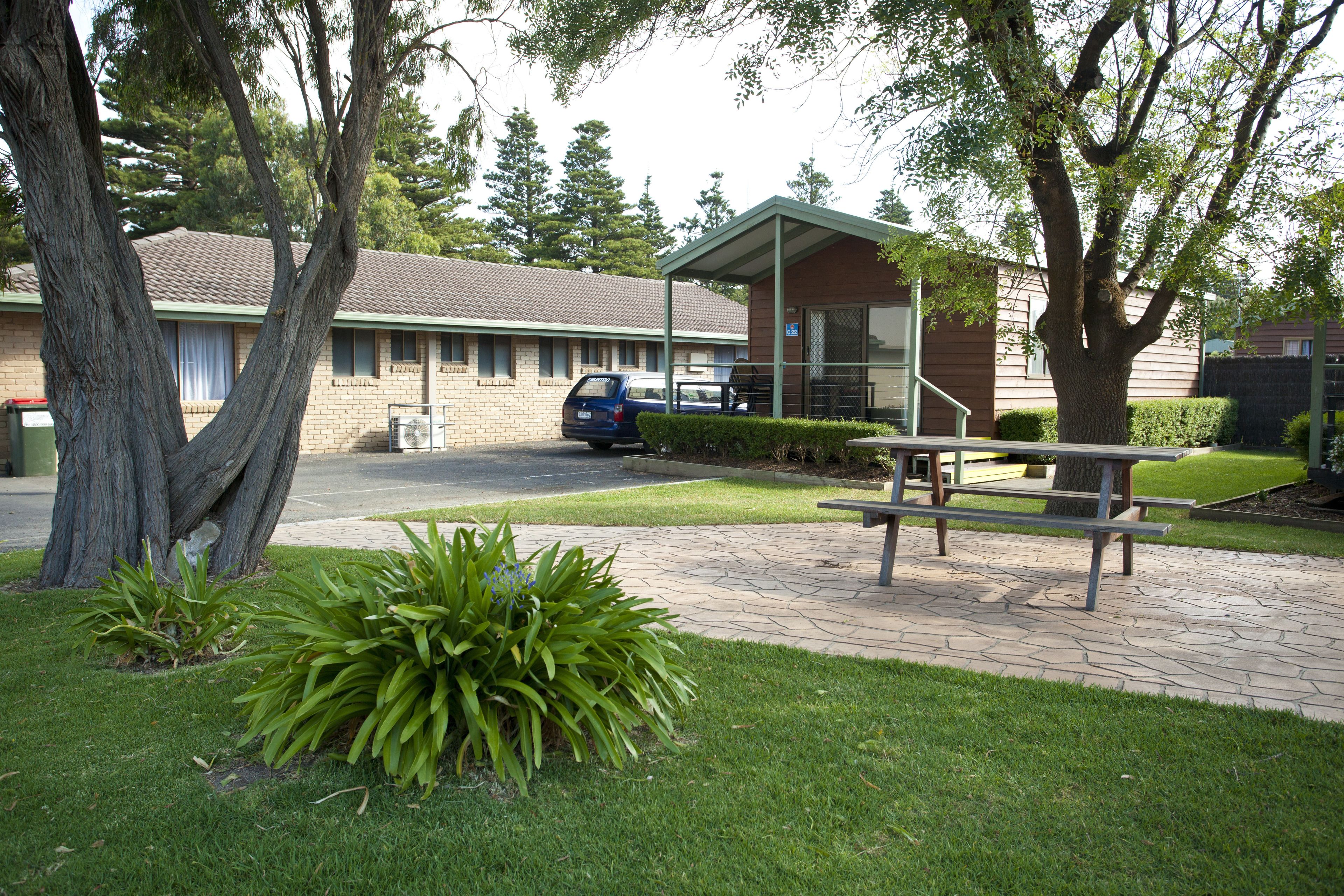A building with a covered picnic area, a car parked in front, and a tree in the foreground.