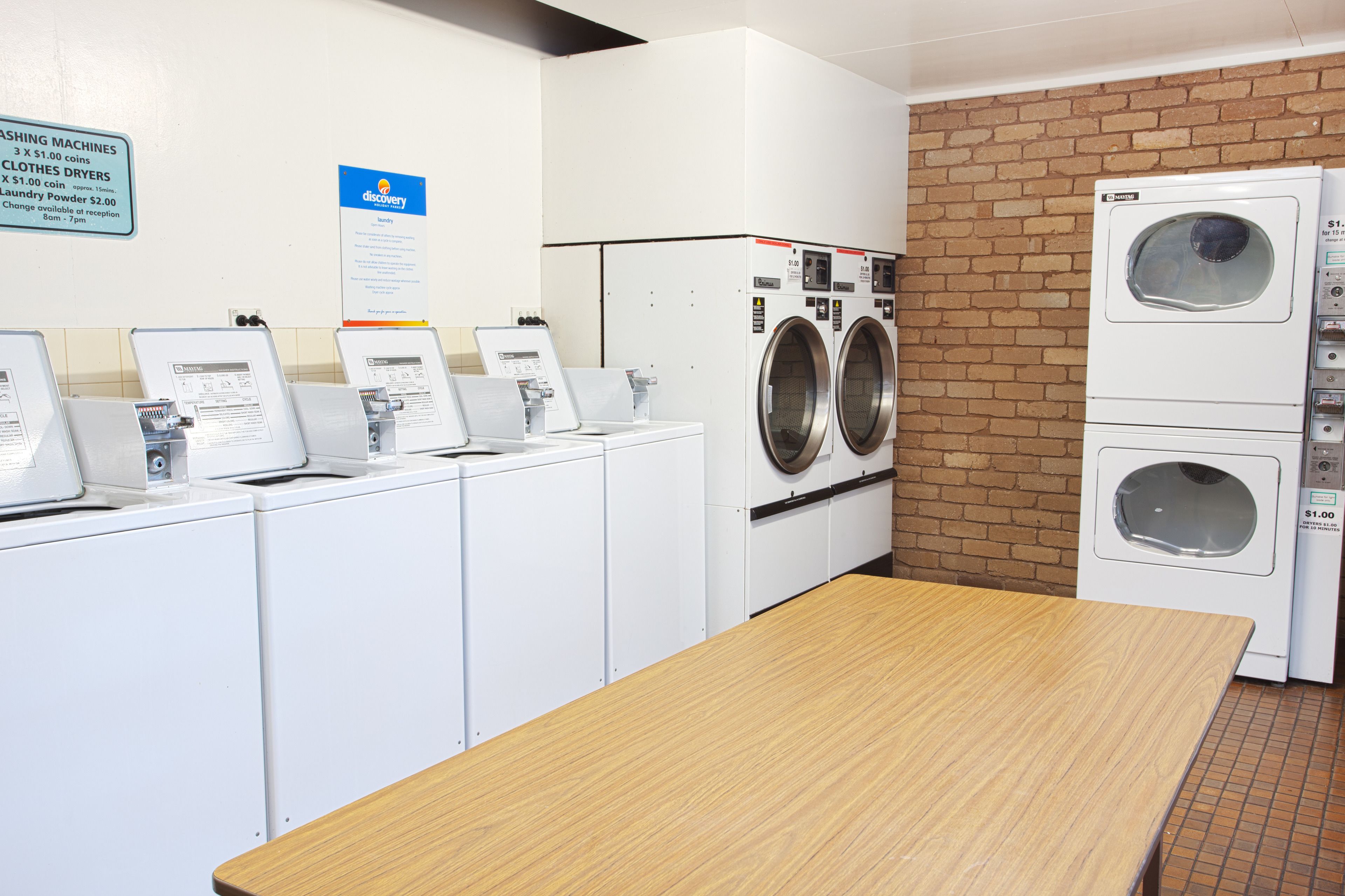 A laundromat with multiple washing machines, a table, and a brick wall.