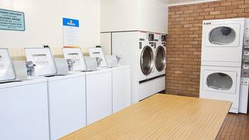 A laundromat with multiple washing machines, a table, and a brick wall.