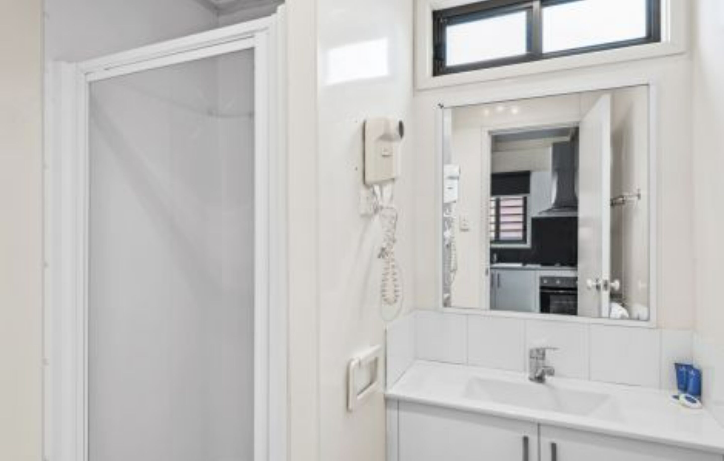 A modern bathroom with a white sink, a mirror, and a shower area.